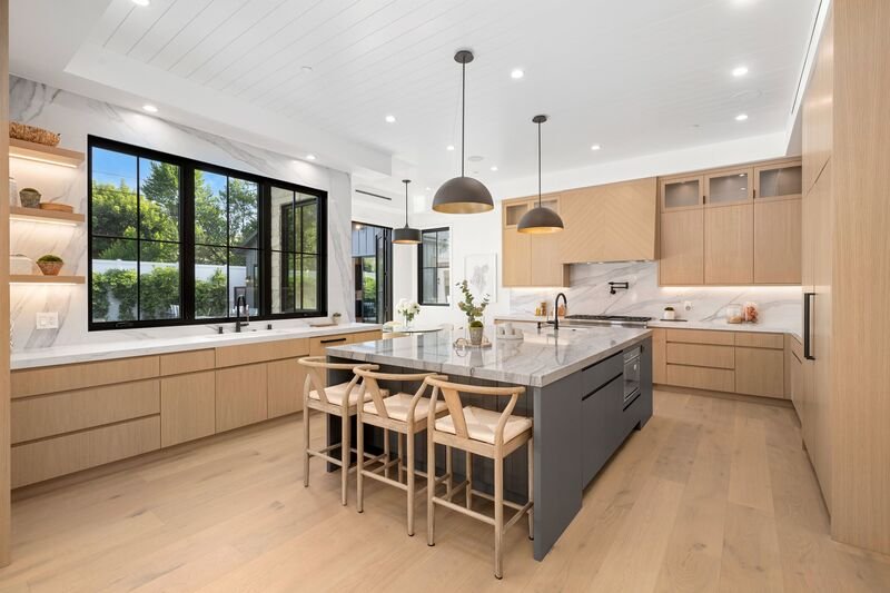 Cocina de madera con toques minimalistas con una barra central con tres sillas y detalles en madera