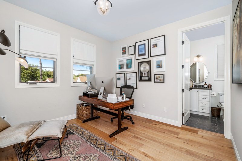 Area de estudio con escritorio y cuadros en una pared y piso de madera de una casa amplia vendida